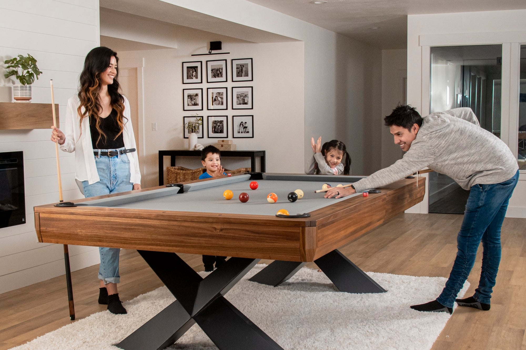 Pool table surrounded by family.  Husband is shooting pool with kids and wife looking
